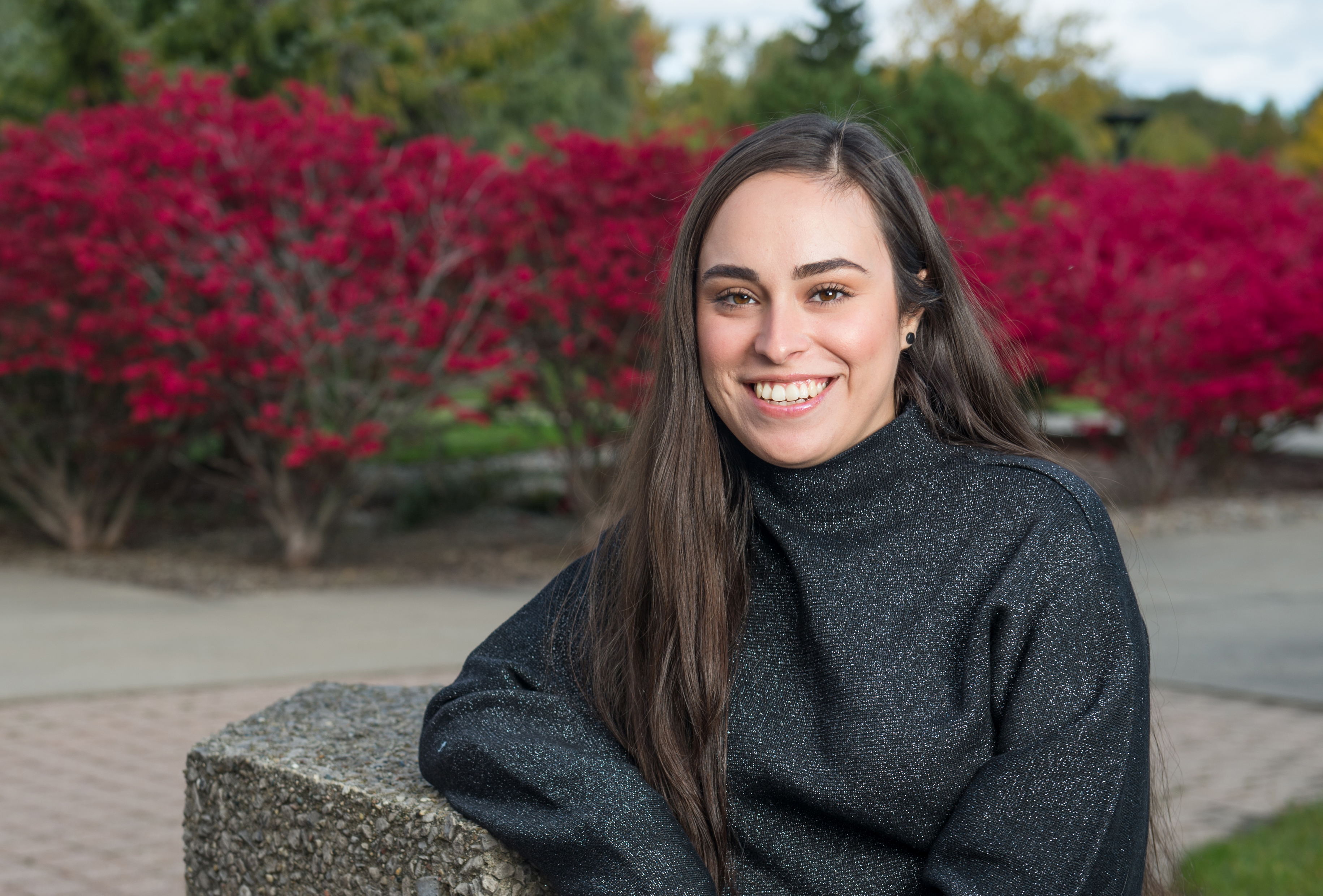 Young woman sitting on bench in front of shrubs with red leaves